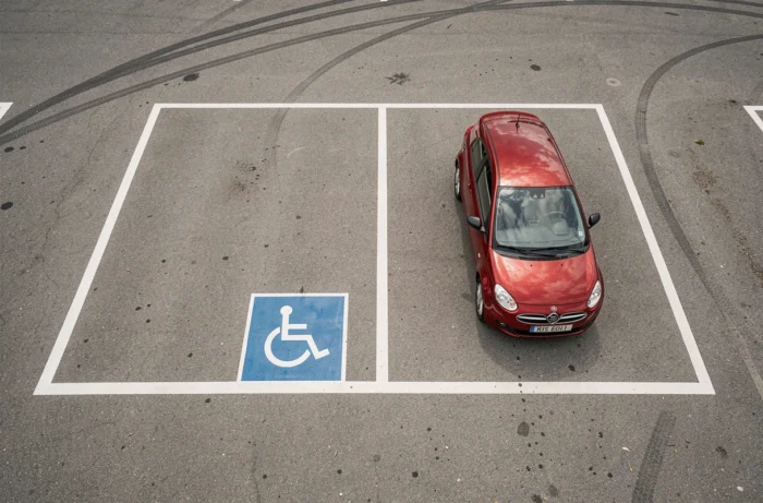 Vue aérienne de deux places de parking réglementaires peintes en blanc sur asphalte dont une place PMR avec marquage bleu
